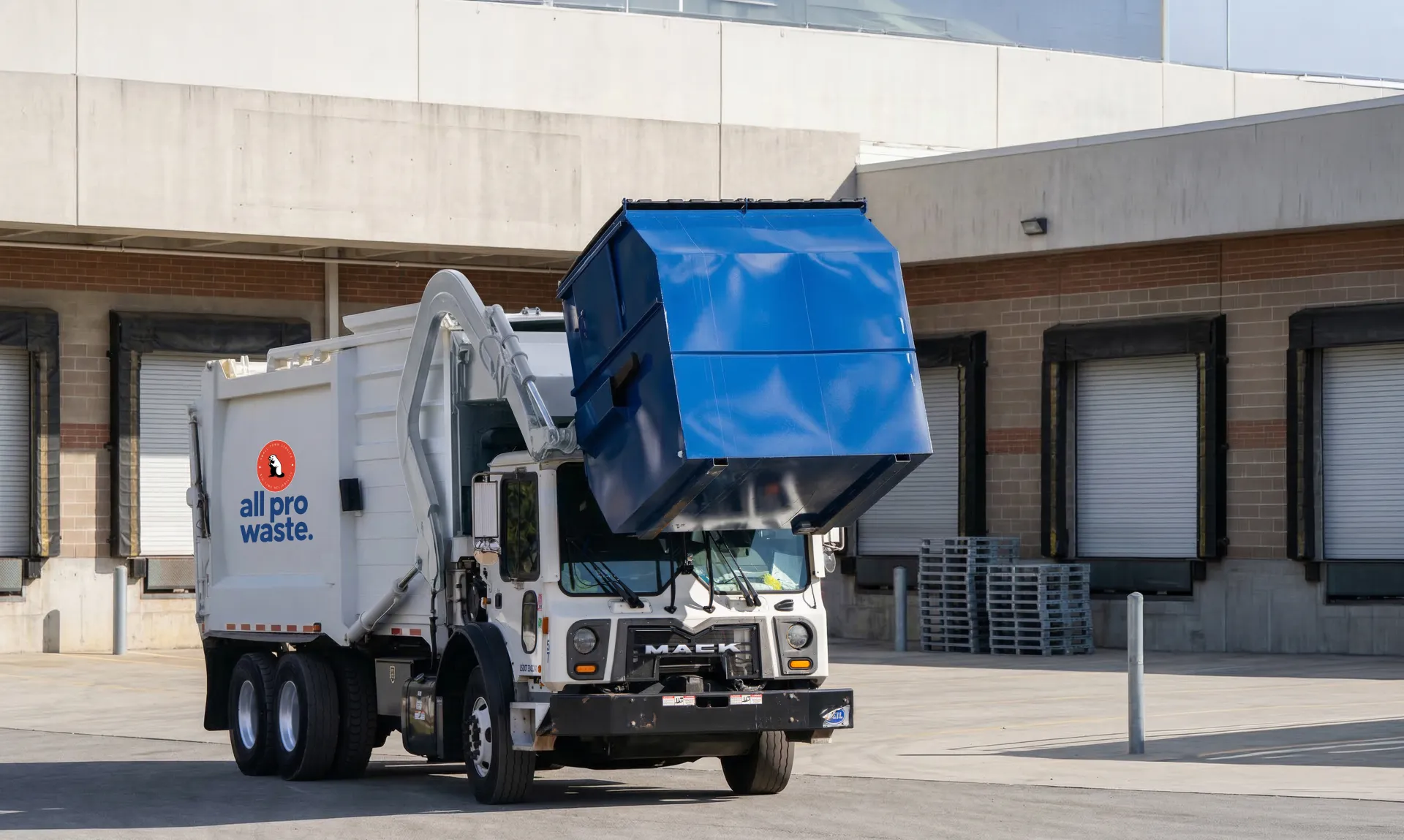 All Pro Waste front-end loader truck servicing a commercial dumpster